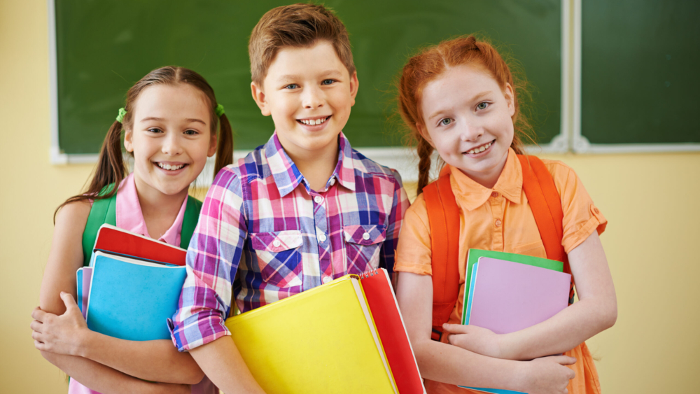 Small group of school friends looking at camera on background of blackboard